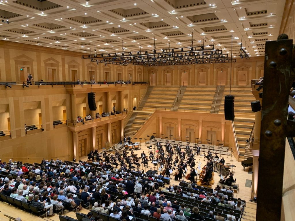 An image of the concert hall with rows of people sitting down.